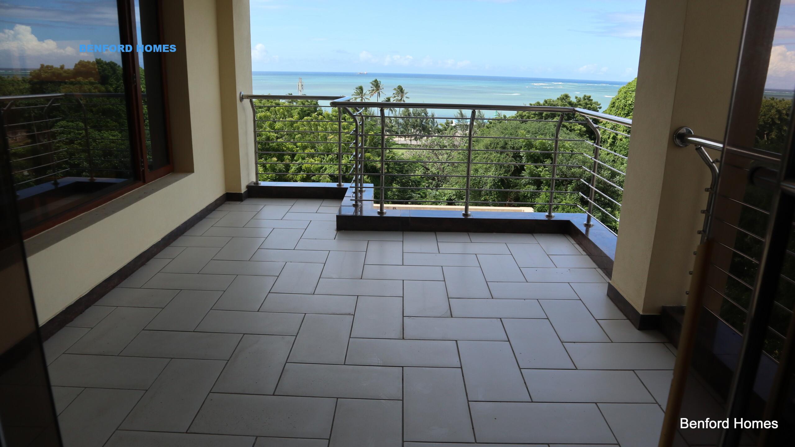 A portion of the balcony's railing frames the scene, hinting a lush canopy of trees and expansive ocean| Benford Homes