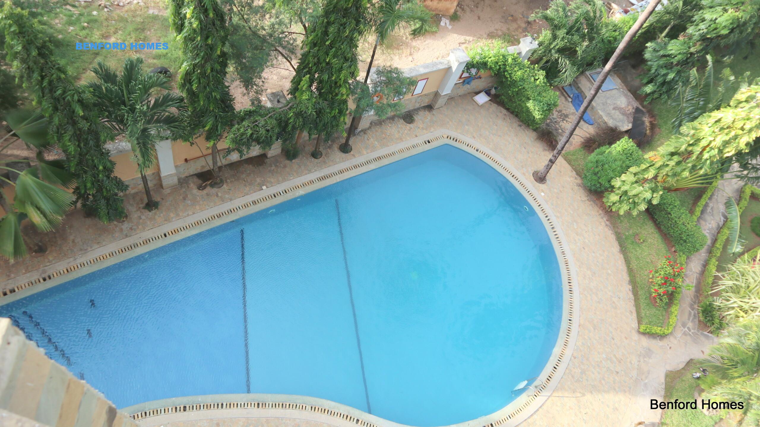 P-shaped swimming pool with tree lined compound and high rise apartments| Benford Homes