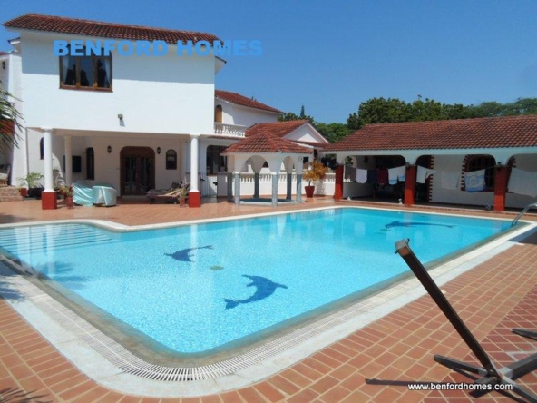 Clear sky blue swimming pool paving to a lavish one storey building in a villa